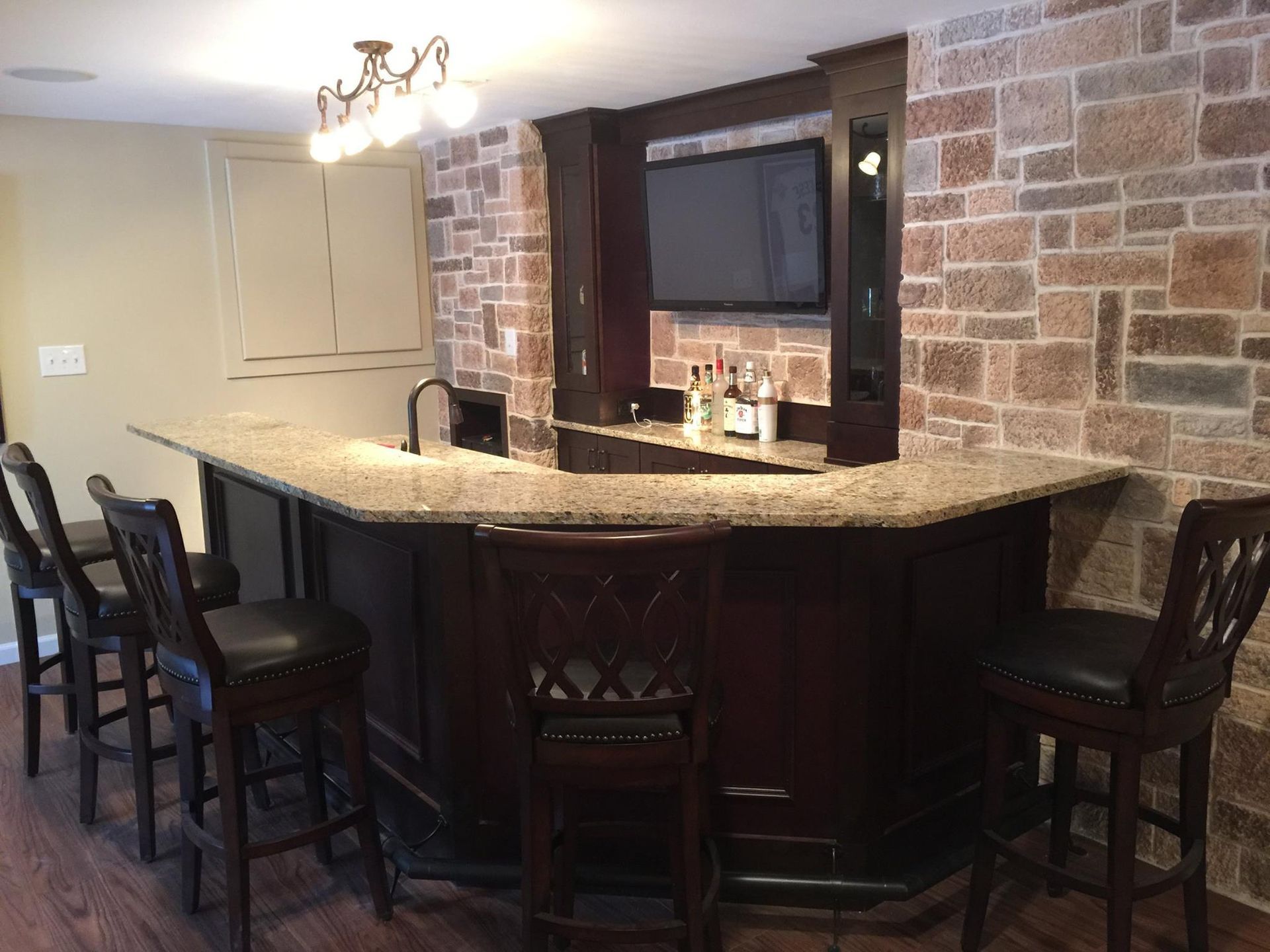 A bar in a basement with a brick wall and a flat screen tv.