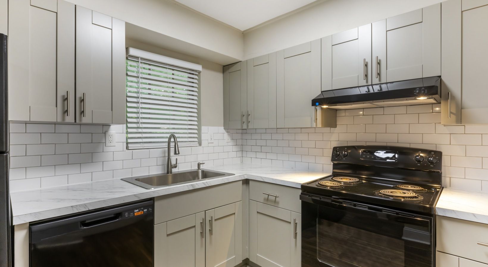 Gray kitchen with black appliances, white subway tile backsplash, and a window.