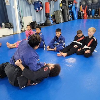 A group of children are sitting on a blue mat in a gym.