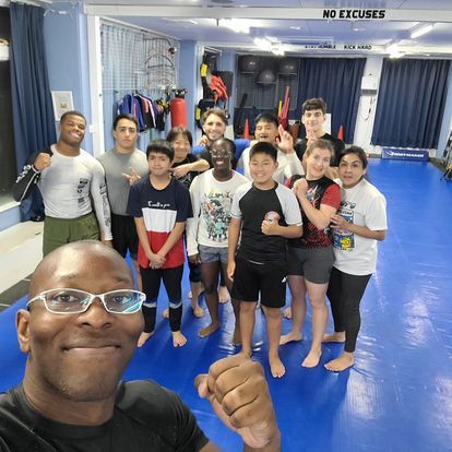 A group of people are posing for a picture in a gym with a sign that says no excuses