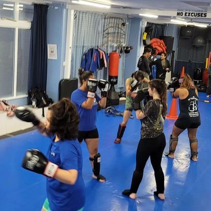 A group of people are boxing in a gym with a sign that says no excuses