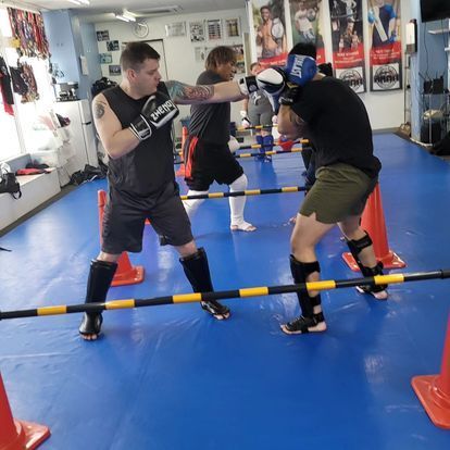 Two men are boxing on a blue mat in a gym