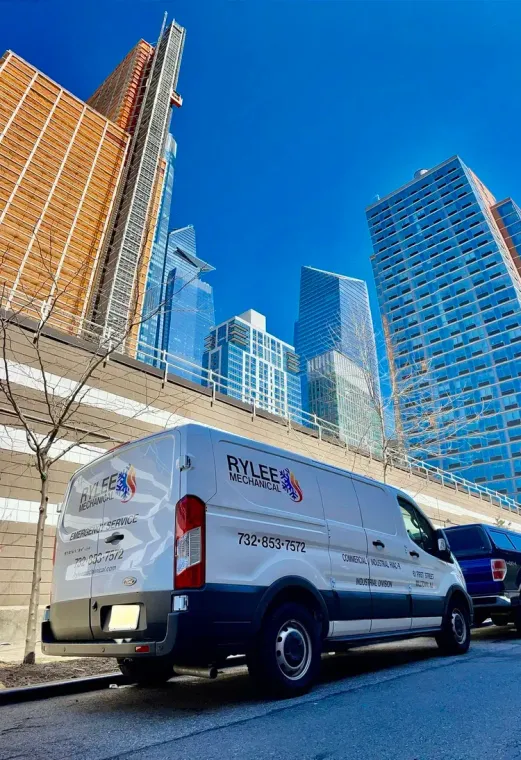 White van on a city street beside tall buildings under a clear blue sky.