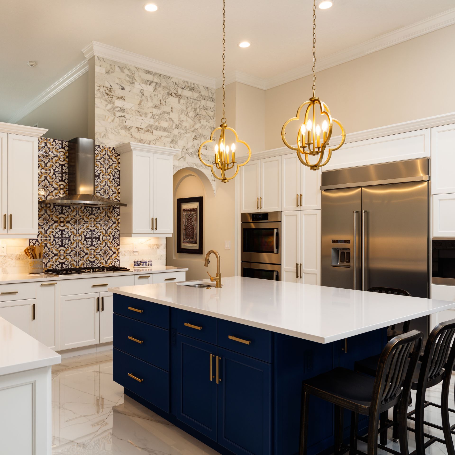 Cuisine moderne avec armoires blanches, îlot bleu, luminaires dorés et appareils électroménagers en acier inoxydable.