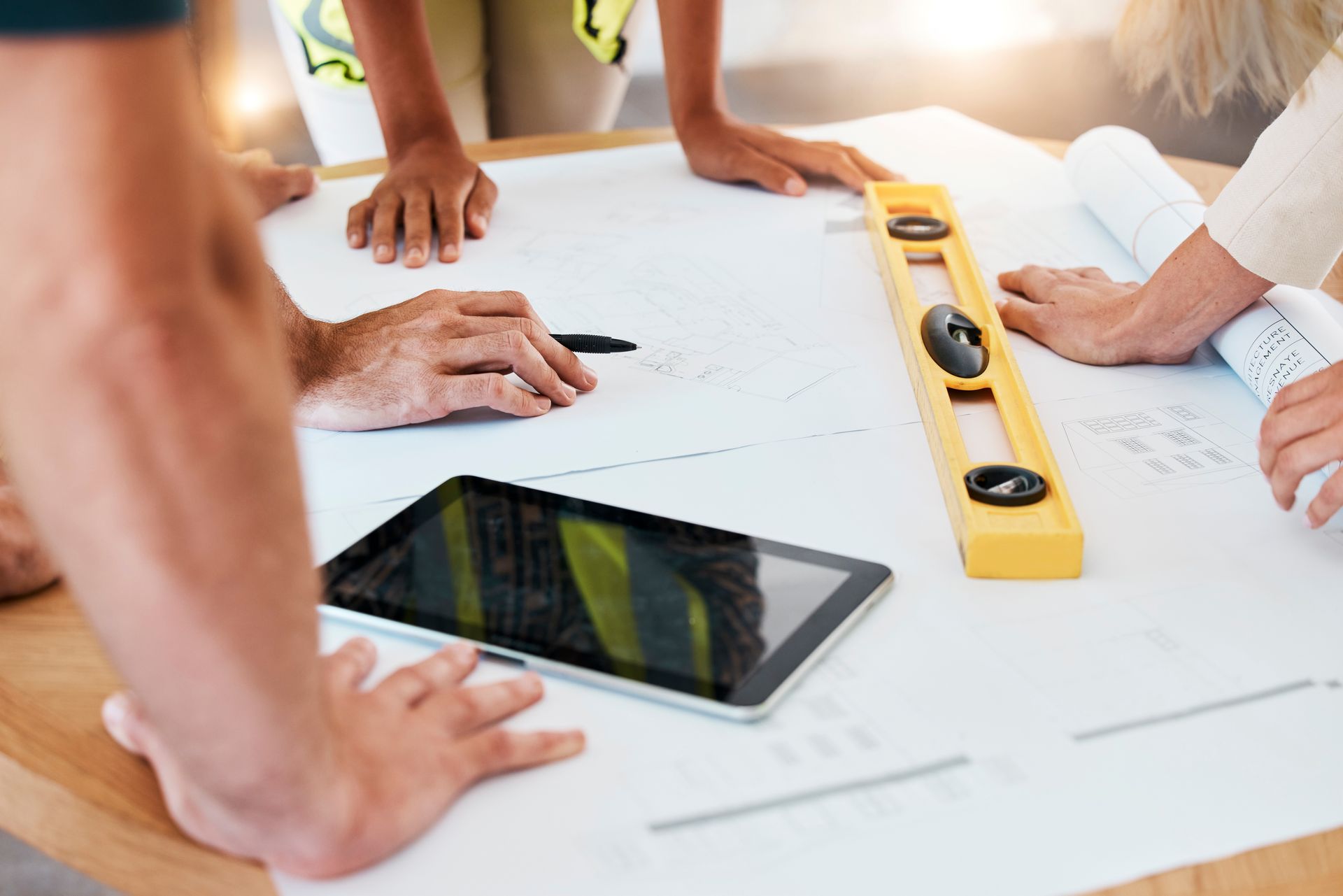 Des personnes travaillant en collaboration sur des plans autour d'une table, à l'aide d'un niveau et d'une tablette.