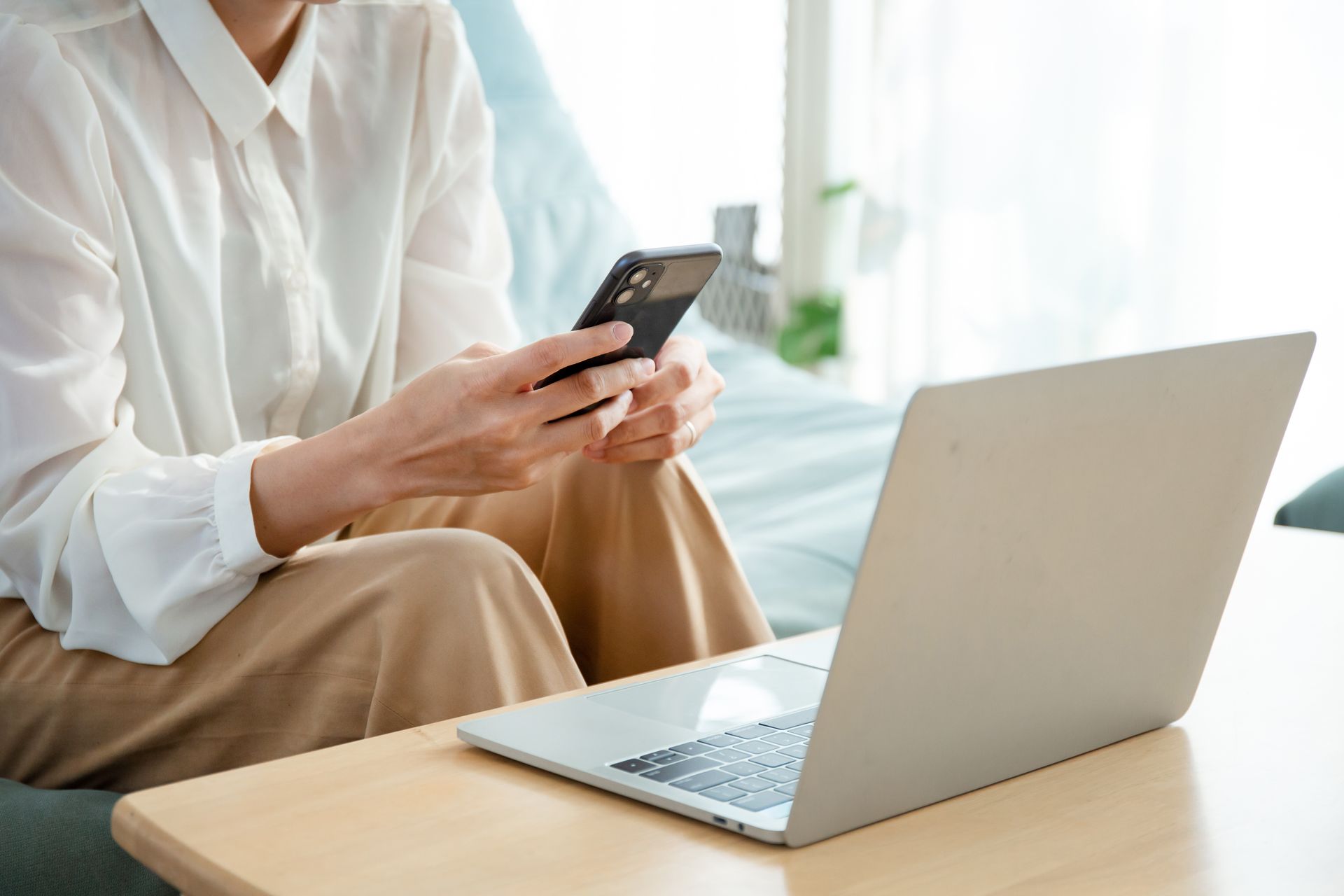 Une femme est assise sur un canapé en utilisant un ordinateur portable et un téléphone portable.