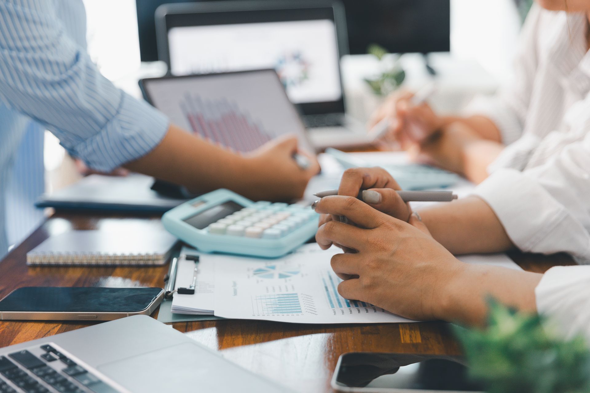 People reviewing financial documents at a table with laptops, calculator, and charts.