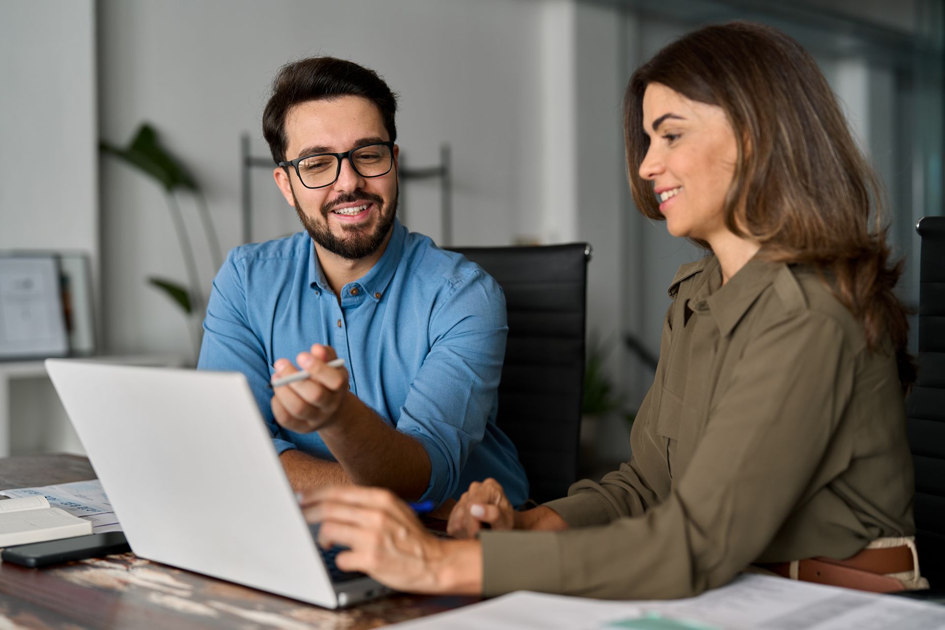 Two people looking at laptop, smiling. Man points while woman types in office.