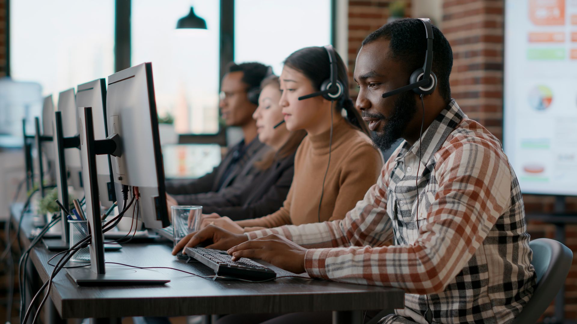People in headsets typing at computers in an office setting.