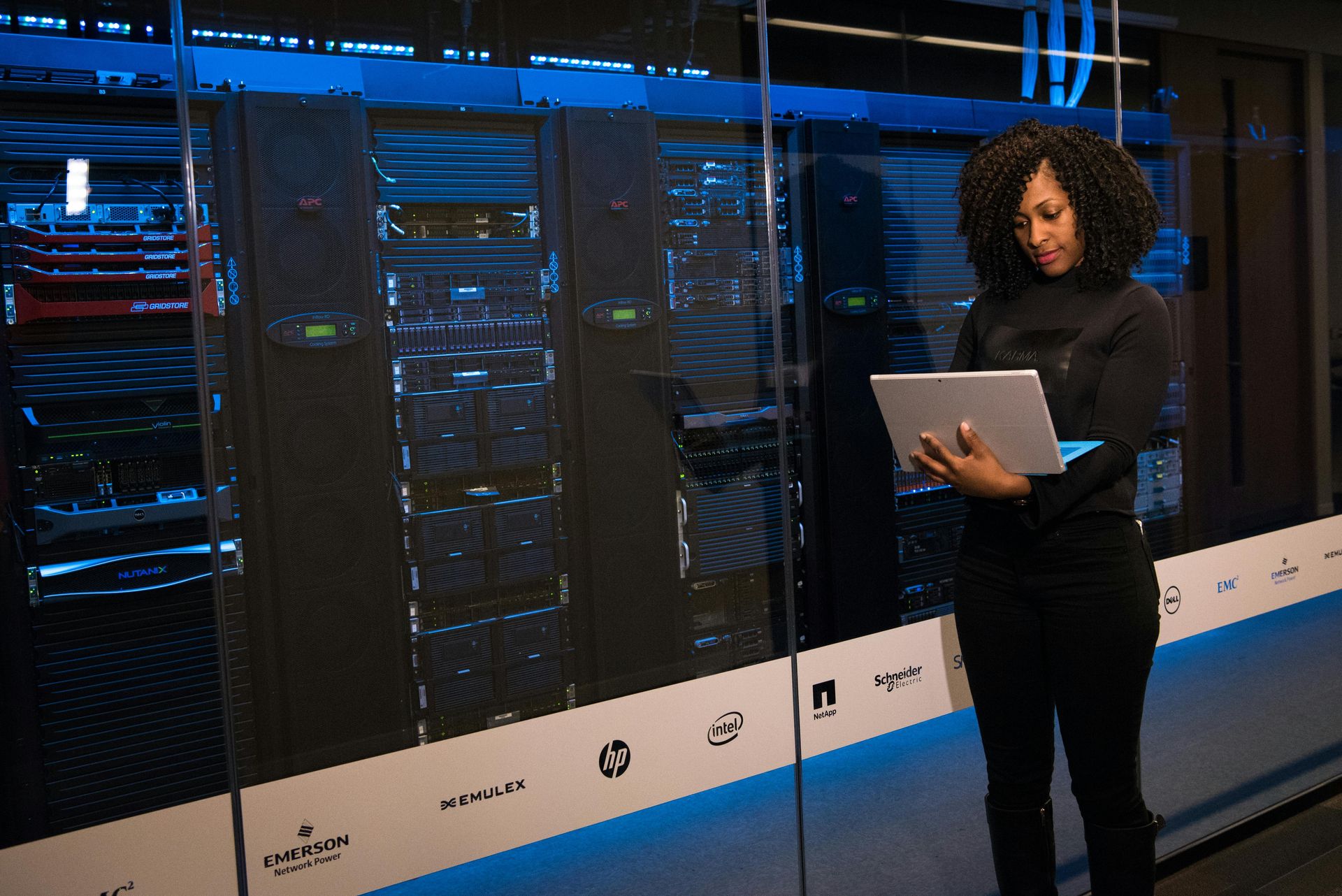 Woman holding tablet, inspecting server racks in a data center, blue lighting, modern setting.