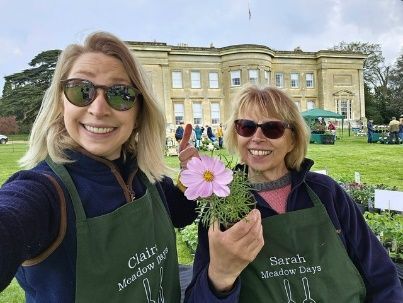 Two women are holding a pink flower in front of a large building.
