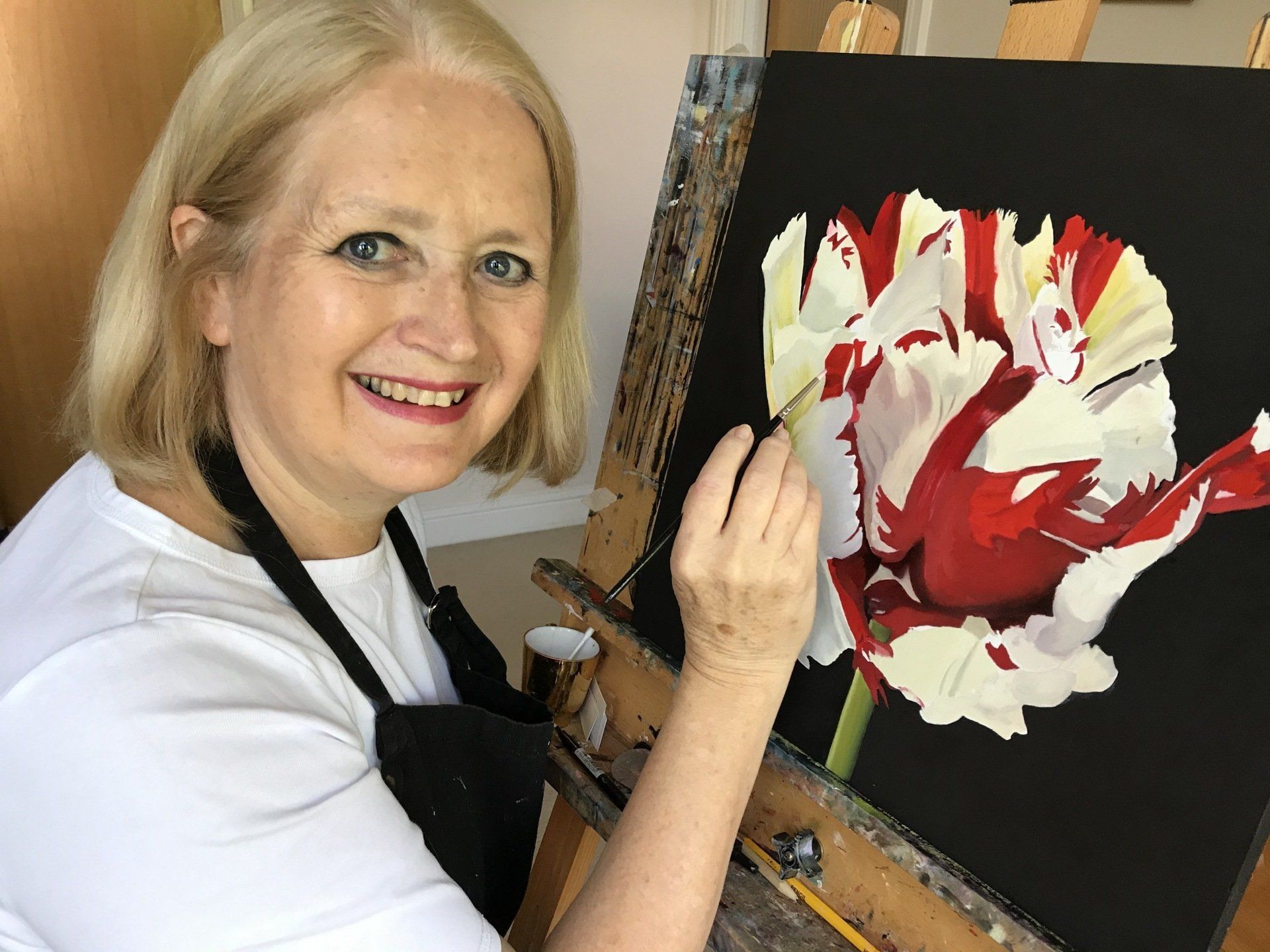 A woman is painting a red and white flower on an easel.