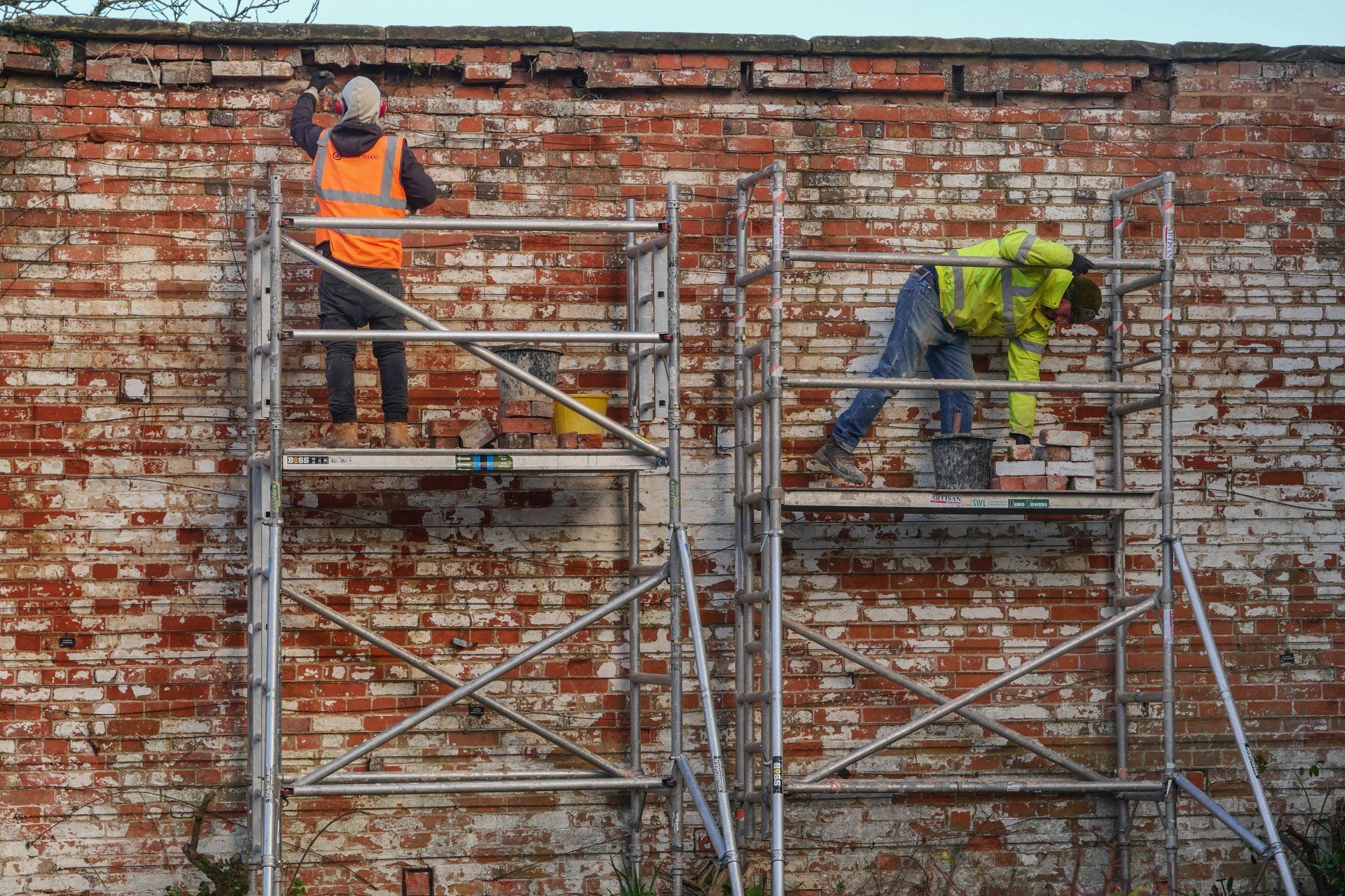 Two men are working on a brick wall on scaffolding.