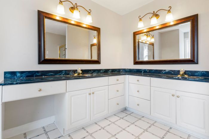 Bright bathroom vanity with double mirrors, brass lights, white cabinets, and blue countertop trim