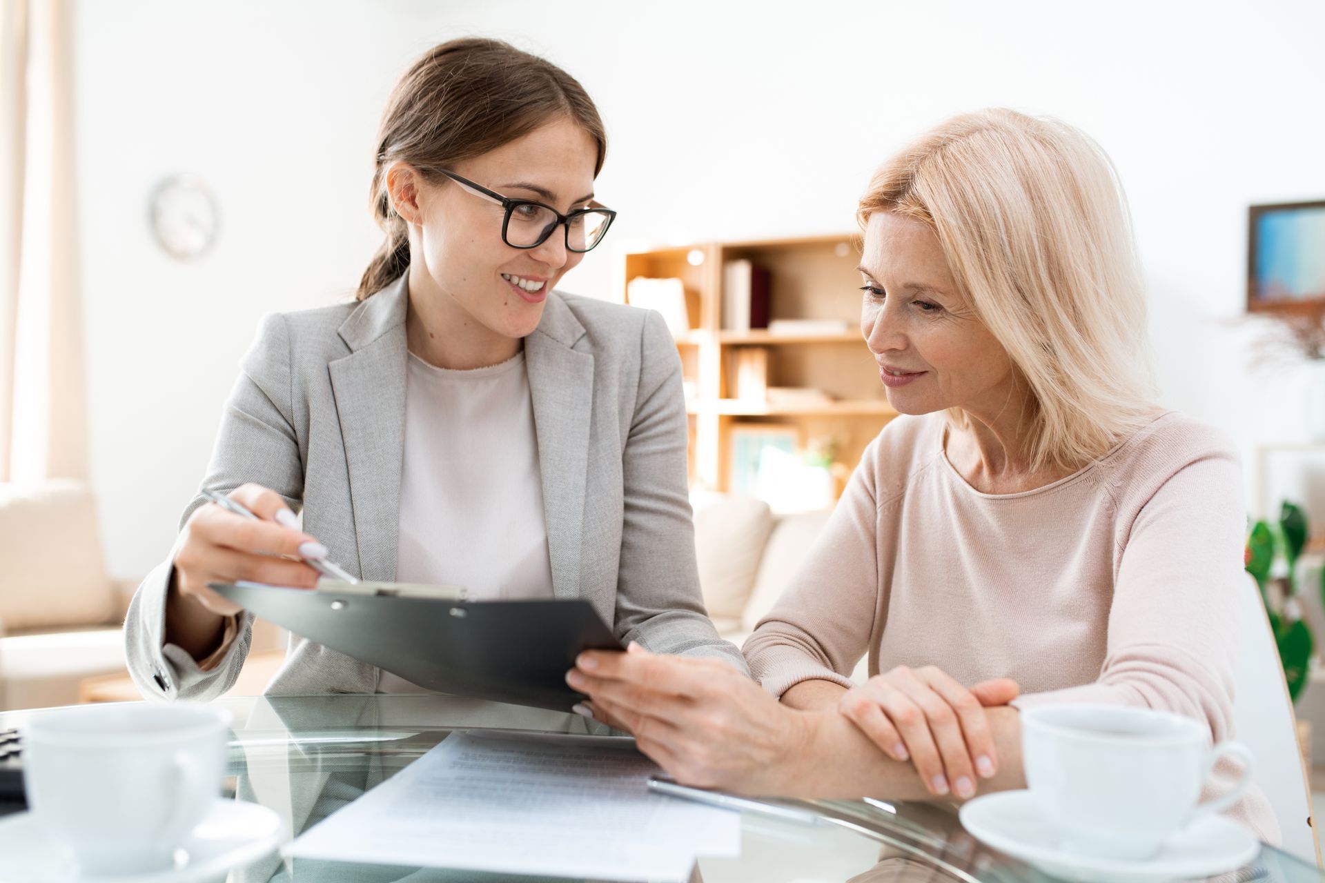 Two women reviewing a document at a desk in a bright office, one holding a tablet and smiling