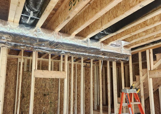 Insulated return and air trunk lines in a new house under construction with a ladder sitting in the room.