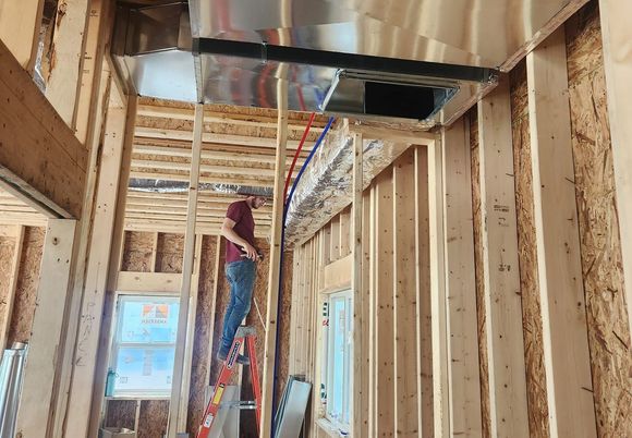 Man on a ladder working on HVAC ducts in new construction.