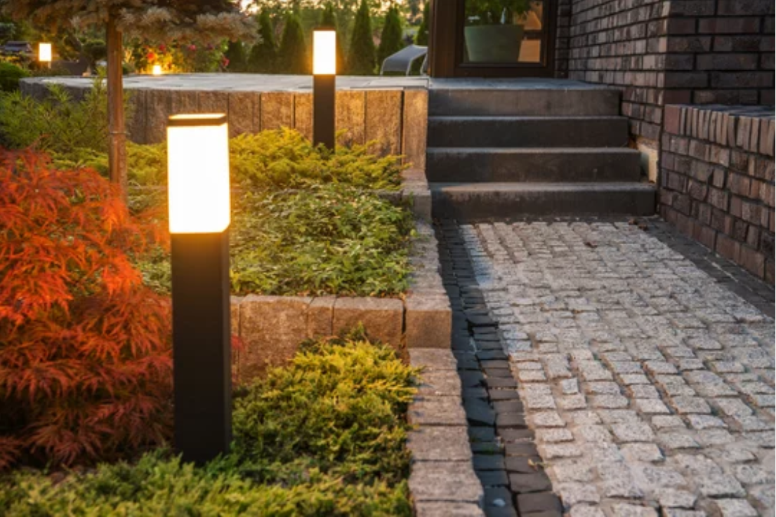 A cobblestone walkway with lights on the side of it leading to a house.