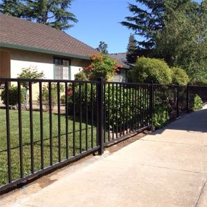 Black wrought iron fence along a sidewalk beside a house and green lawn under a clear blue sky