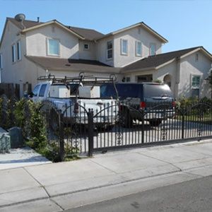 Two trucks parked behind a black wrought iron gate in front of a beige two-story house