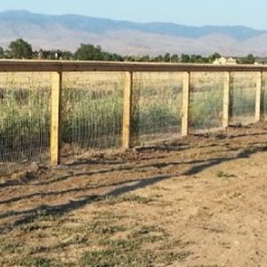 Wooden fence along a dry dirt path with grassy field and mountains in the background