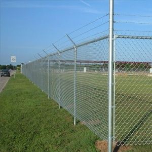 Chain link fence along a roadside beside a grassy airfield under a clear blue sky