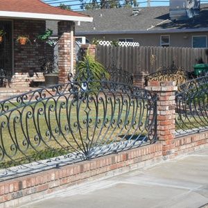 Brick and wrought iron front yard fence beside a house and sidewalk