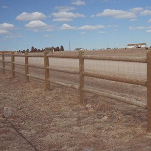 Wooden fence beside a dry field under a partly cloudy blue sky