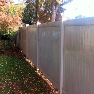 White fence along a leaf-covered path beside autumn trees in sunlight