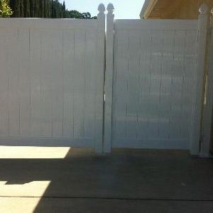 White vinyl double driveway gate in front of a concrete driveway, with sunlight and shadows.
