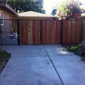 Concrete driveway ending at a wooden gate with a black side gate beside a house