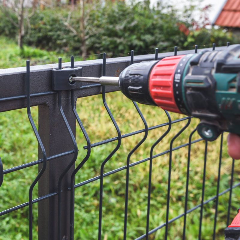 A drill fastening a black metal fence post in a grassy yard