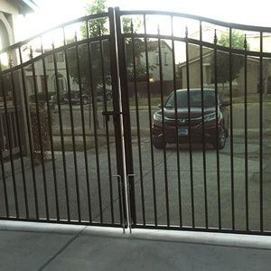 Black wrought iron gate in front of a driveway with a parked car and house beyond.