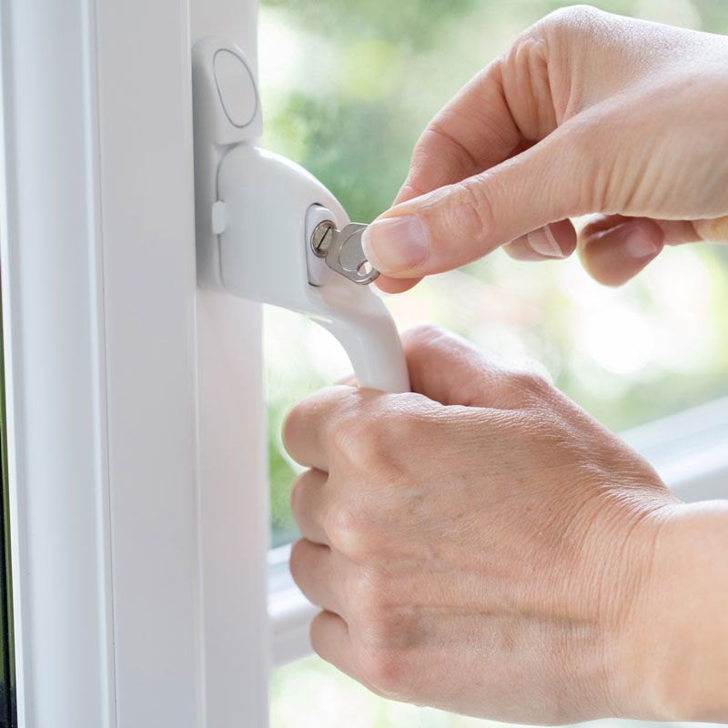 Hands locking a white window latch on a bright window frame