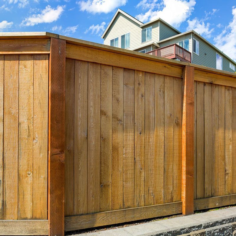 Wooden privacy fence with a house visible above it under a blue sky.