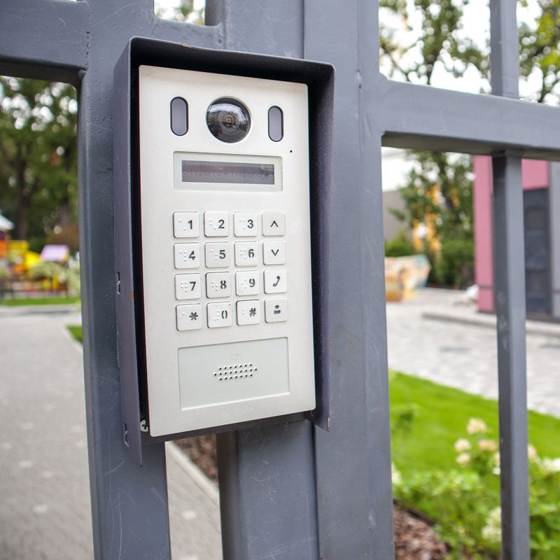 Outdoor intercom keypad on a metal gate, with camera and speaker panel.