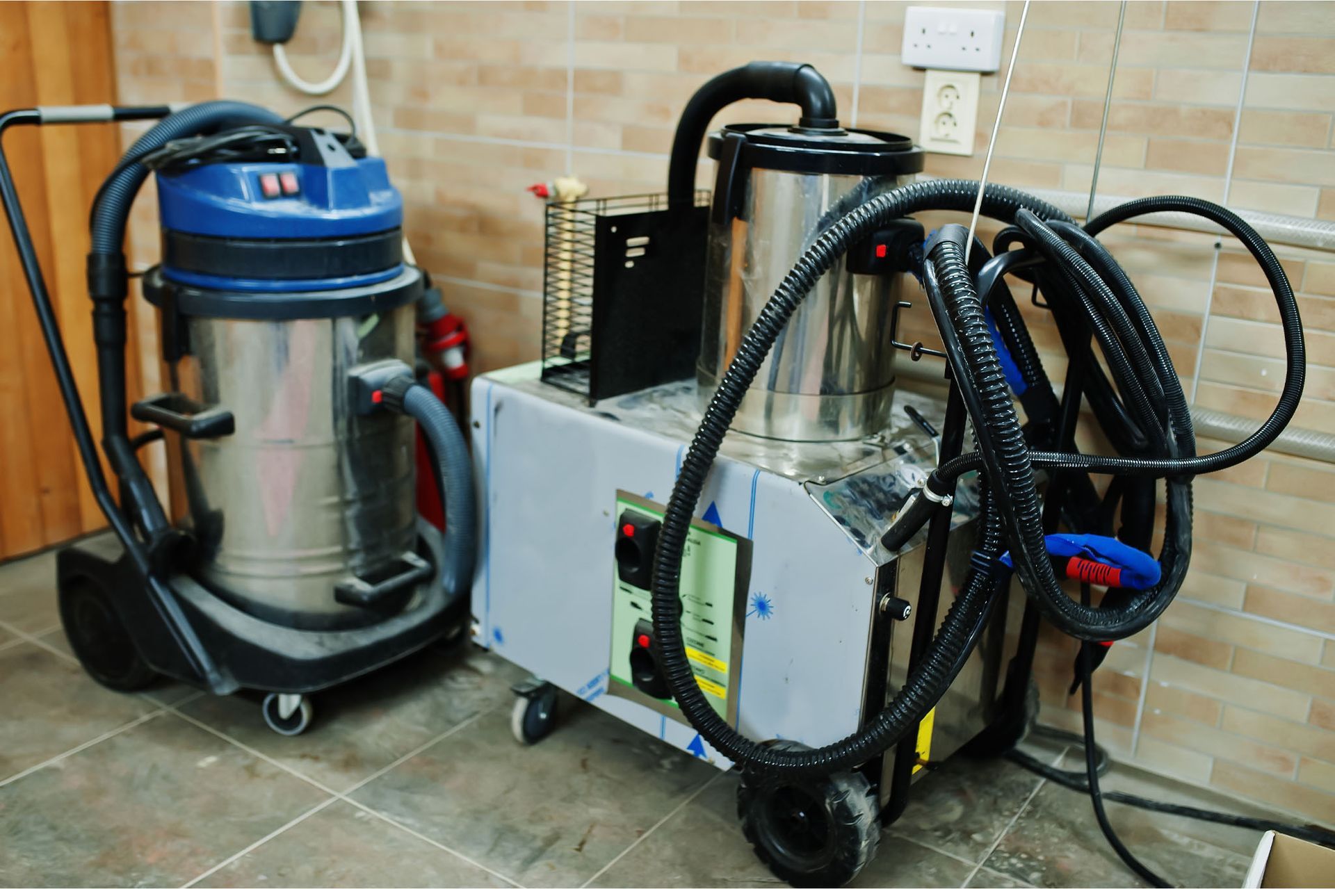 Two vacuum cleaners are sitting next to each other on a tiled floor.