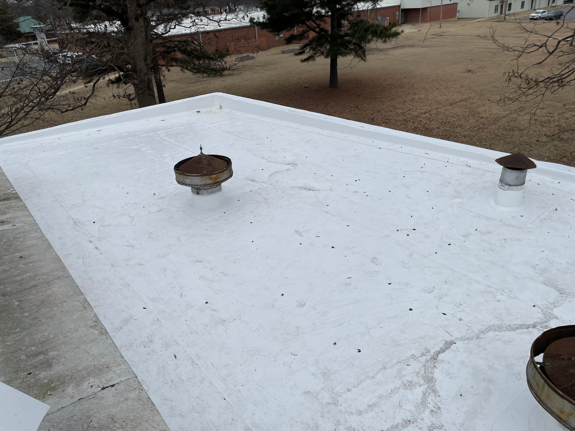 White flat roof with three small vents and a snowy yard in the background
