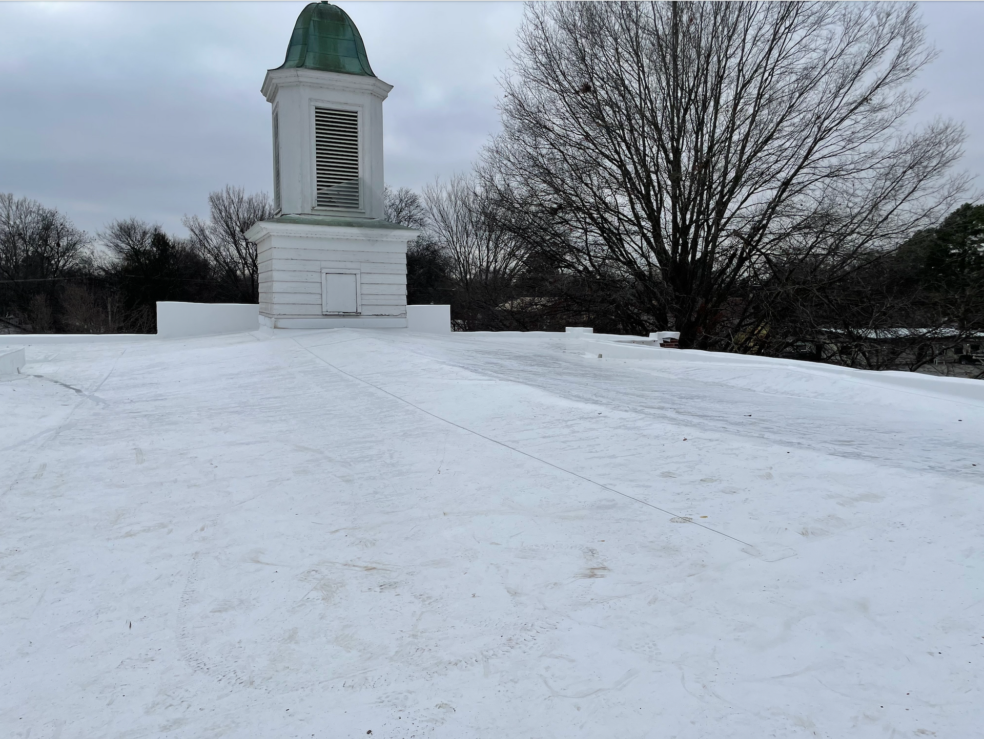 Snow-covered monument with a green-domed statue under a cloudy winter sky