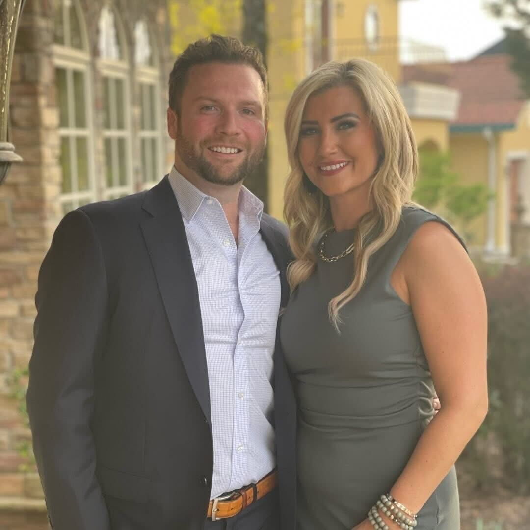 Smiling couple posing outdoors in formal attire on a sunlit street