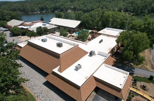 Aerial view of white-roofed buildings beside a lake and trees.