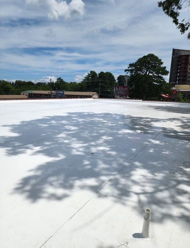 White rooftop under a blue sky with tree shadows and a small vent in the foreground