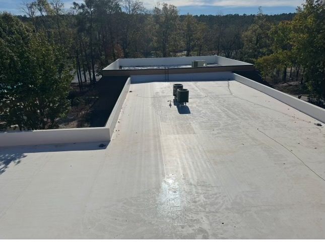 Flat white rooftop with vents, surrounded by trees under a clear sky