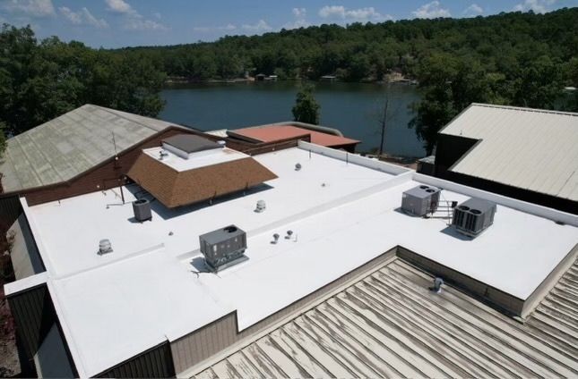 Rooftop HVAC units on a white flat roof beside a lake and wooded shoreline