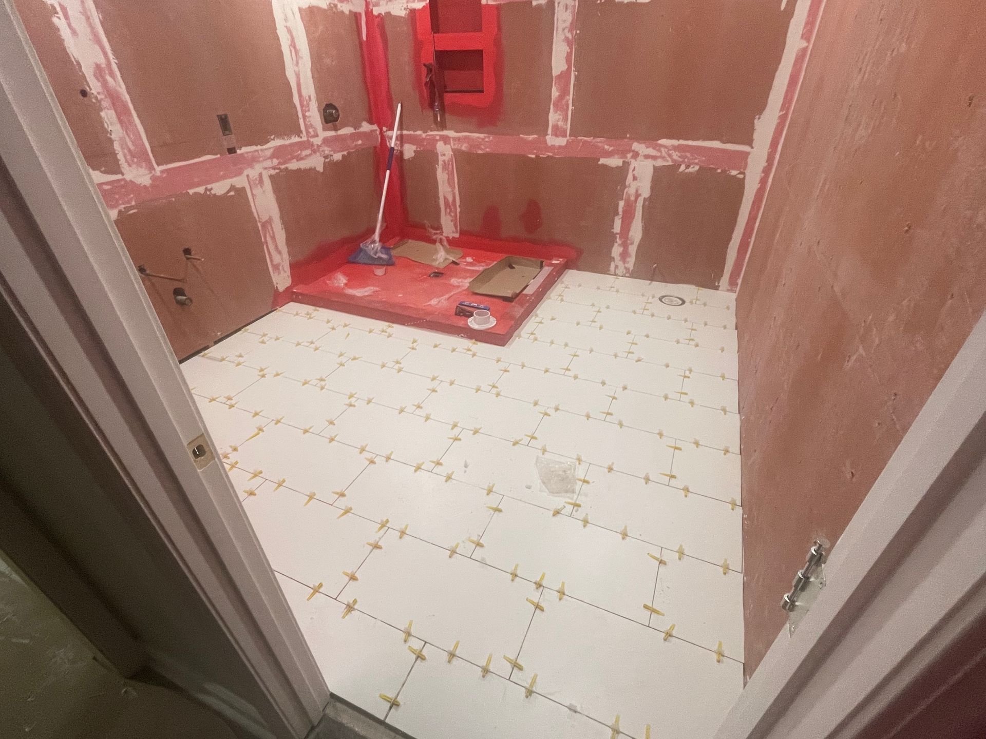Partially tiled bathroom under construction with red wall panels and a white tiled floor