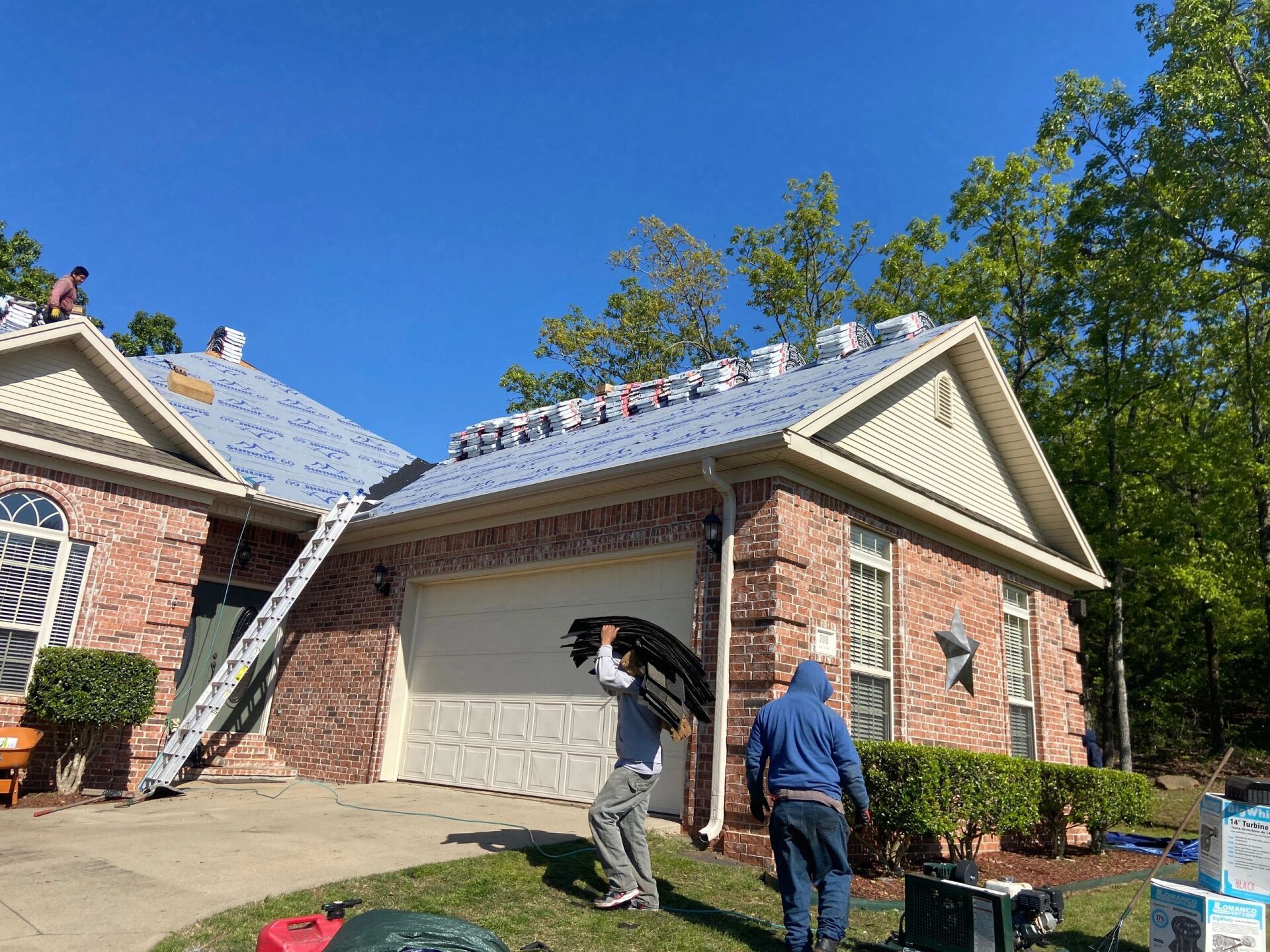 Two people inspect a brick house roof and garage on a sunny day.