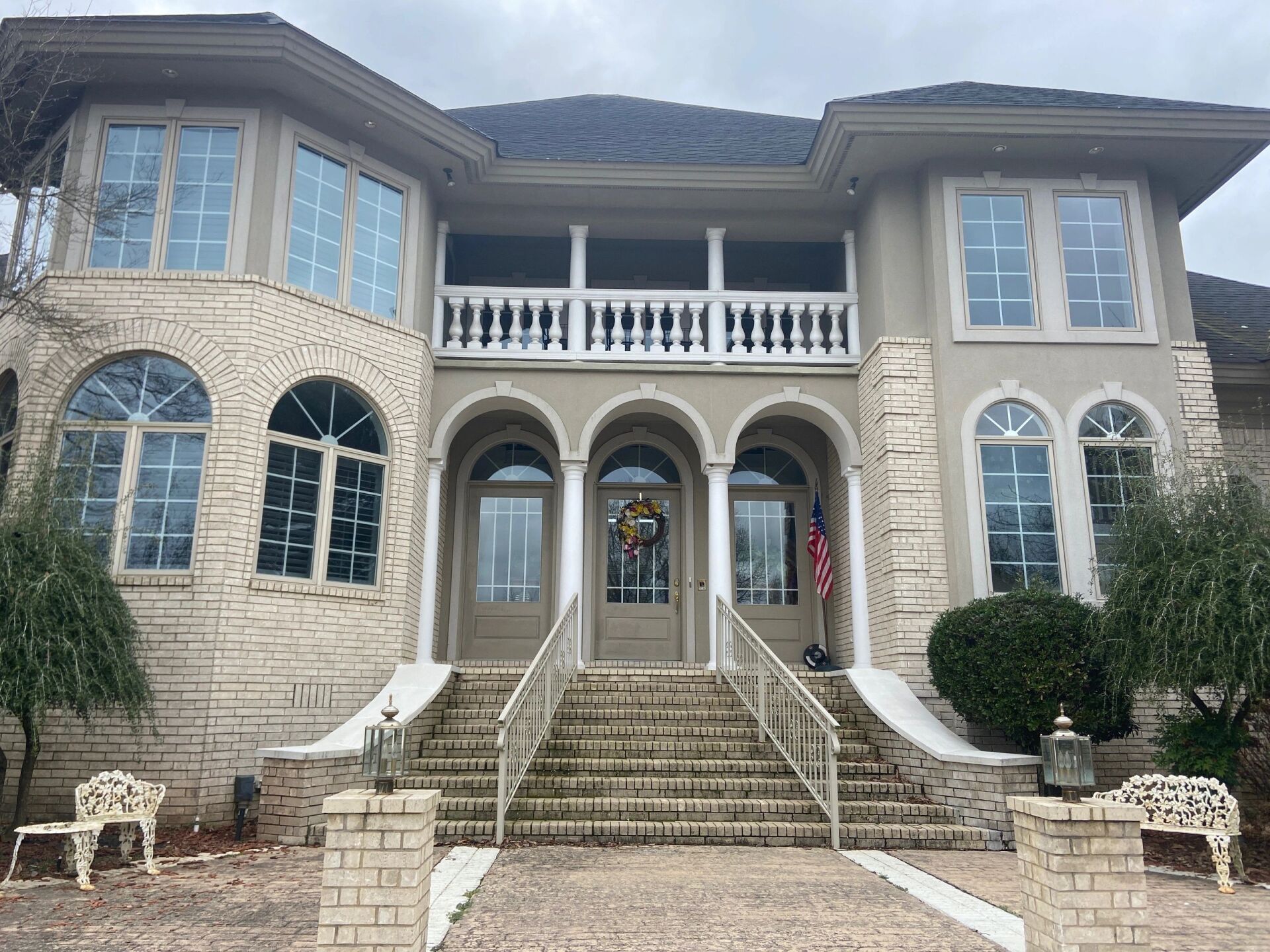 Large stone mansion with arched windows, central staircase, and a balcony above the front entrance.