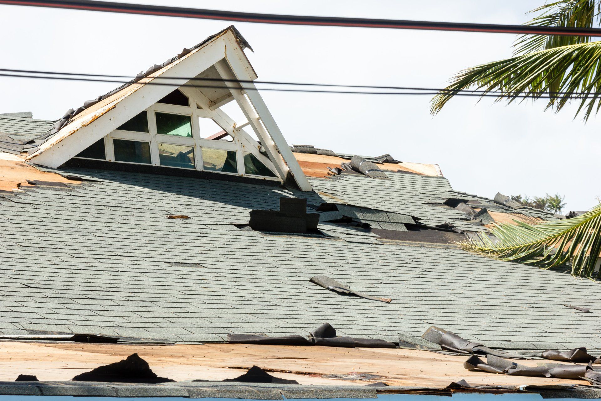 Damaged gray roof with torn shingles and a broken dormer after storm damage