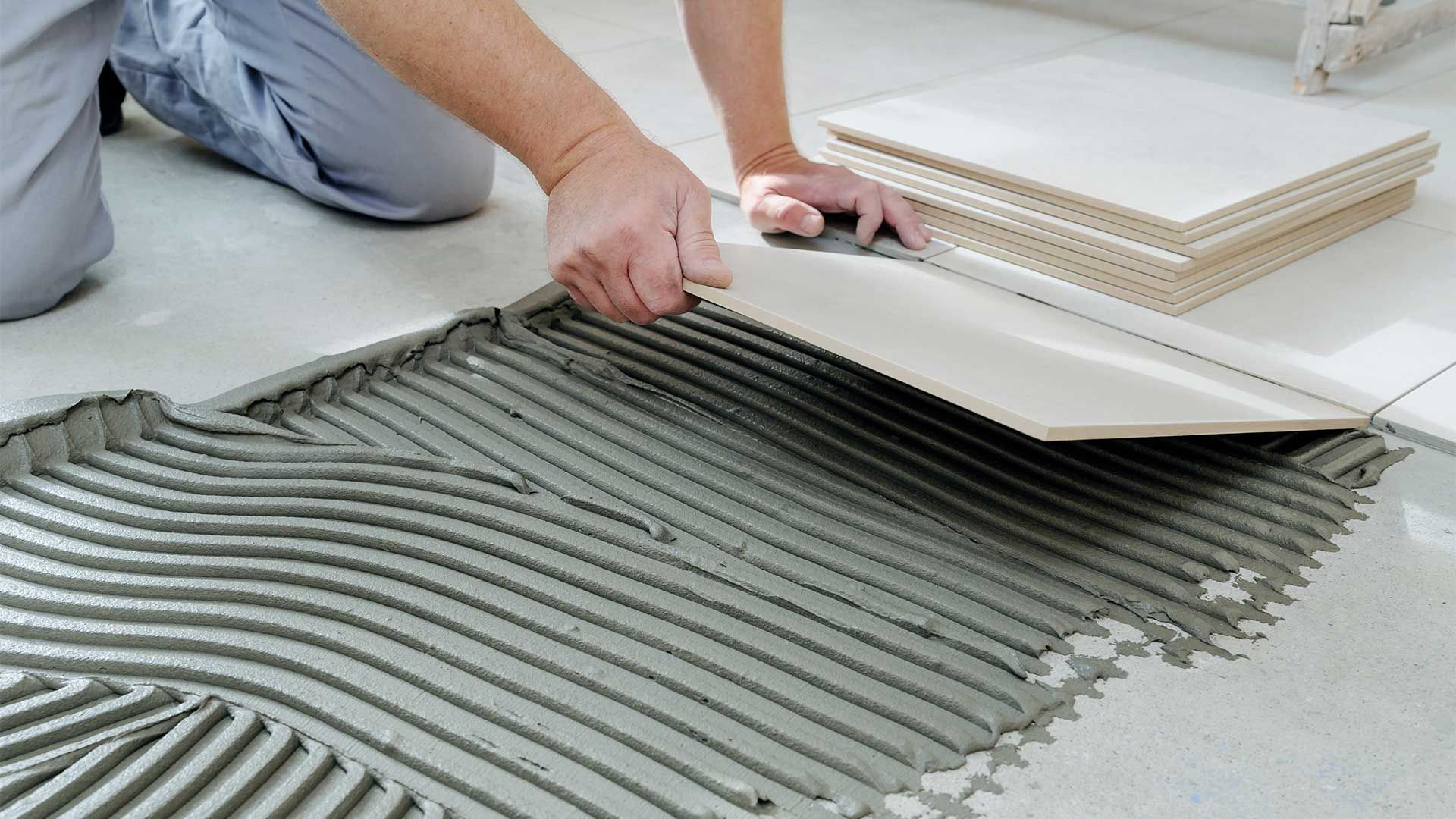 A person is laying tiles on the floor with a trowel.