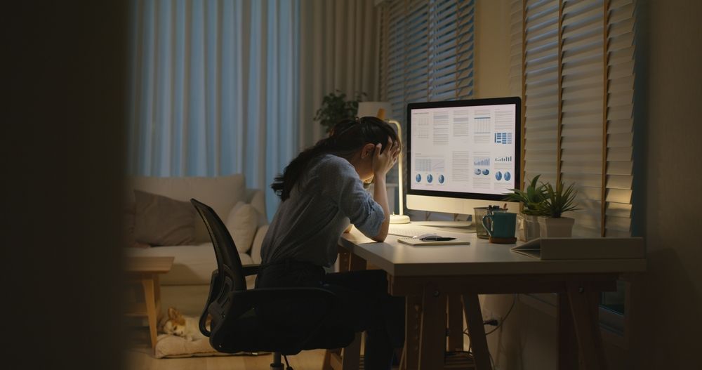 a woman is sitting at a desk with her head in her hands in front of a computer in a brownout.